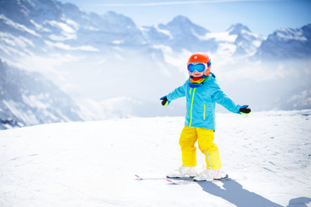 Child skiing in the mountains. Kid in ski school. Winter sport for kids. Family Christmas vacation in the Alps. Children learn downhill skiing. Alpine ski lesson for boy or girl. Outdoor snow fun.の写真素材
