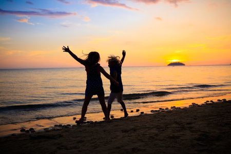 Child playing on ocean beach. Kid jumping in the waves at sunset. Sea vacation for family with kids. Little boy and girl running on tropical beach of exotic island during summer holiday.の写真素材