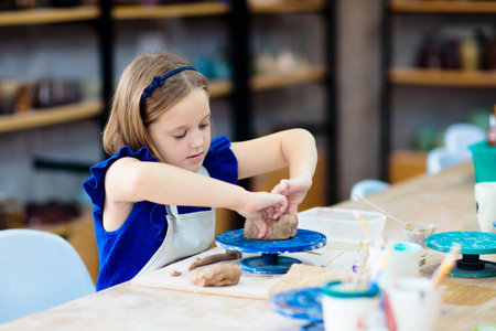 Child working on pottery wheel. Kids arts and crafts class in workshop. Little girl creating cup and bowl of clay. Creative activity for young children in school. Cute kid forming toy with ceramic.の写真素材