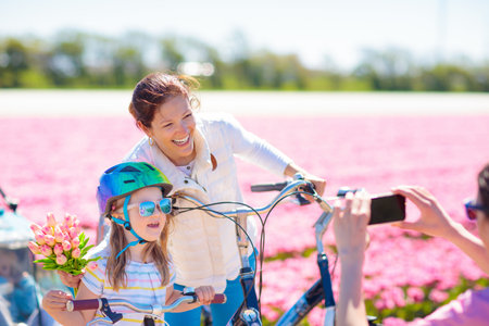Dutch family riding bicycle in tulip flower fields in the Netherlands. Mother and kids taking selfie picture with mobile phone camera on bikes at blooming tulips in Holland. Parents and children biking.の写真素材
