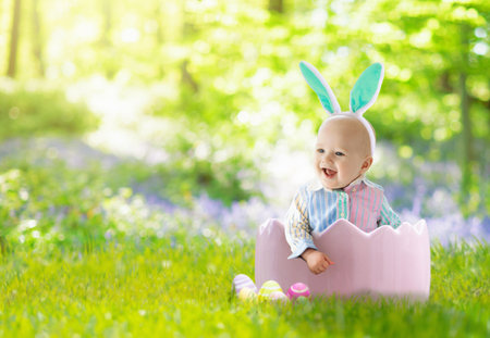 Child on Easter egg hunt. Baby boy with bunny ears sitting in white basket with colorful eggs. Kid with colored eggs. Easter decoration, family celebration, Christian traditions. Cute toddler.の写真素材