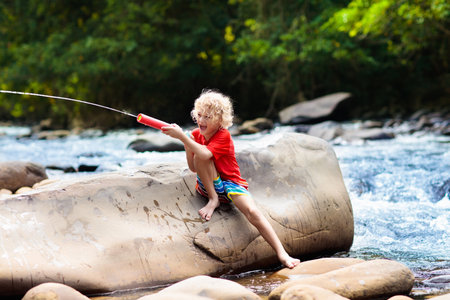 Children hiking in Alps mountains crossing river. Kids play in water at mountain in Austria. Spring family vacation. Little boy and girl on hike trail. outdoor fun. Active recreation with children.の写真素材