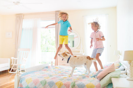 Child jumping on bed in white bedroom with big window. Kids play at home. Fun jump on parents bed. Room and interior design. Boy at home. Sunny morning, weekend family relaxing time.の写真素材