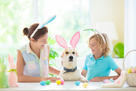Mother and child color Easter eggs. Funny dog with bunny ears. Little boy and mom dye eggs. Easter egg hunt. Family celebration and home decoration for spring holiday.の写真素材