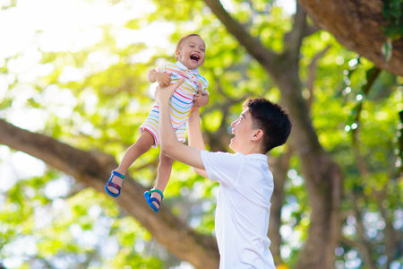 Teenage Asian boy playing with his baby brother. Brothers have fun in summer park. Siblings with big age difference. School child hugging little sibling. Kids bonding and love.の写真素材