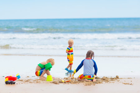 Child playing on tropical beach. Little girl and boy digging sand at sea shore. Family summer holidays. Kids play with water and sand toys. ocean and island fun. Travel with young children.の写真素材