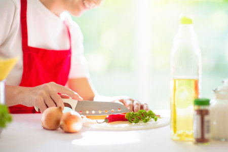 Family cooking dinner. Woman making spaghetti in white sunny kitchen. Italian meal preparation. Pasta and vegetables for vegetarian healthy lunch. Female cutting tomato for noodle sauce.の写真素材