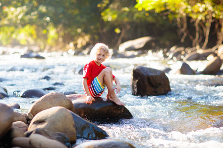 Children hiking in Alps mountains crossing river. Kids play in water at mountain in Austria. Spring family vacation. Little boy on hike trail. outdoor fun. Active recreation with children.の写真素材