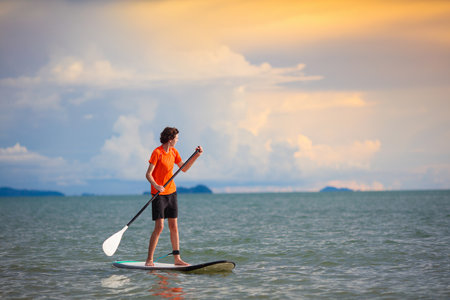 Young man standing up paddle board. Water fun and beach sport. Healthy outdoor sports for summer vacation on tropical island. holiday activity. Fit teenager boy training. Surfer exercising.の写真素材
