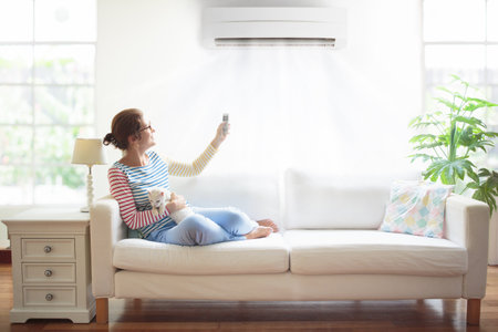 Woman with air conditioner remote control. Comfortable temperature at home. Cooling and heating device. Air conditioning on hot summer day. Female on white couch under cold air breeze.の写真素材