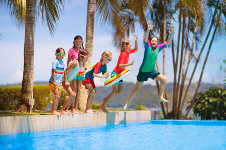 Group of kids jump into swimming pool. Summer water fun. Children play in outdoor pool. Summer family vacation with young kid. Holiday in tropical resort. Travel with child.の写真素材