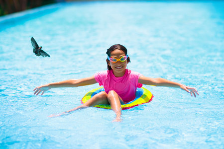 Child in swimming pool floating on toy ring. Kids swim. Colorful rainbow float for young kids. Little girl having fun on family summer vacation in tropical resort. Beach and water toys. Sun protection.の写真素材