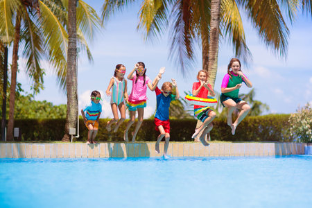 Group of kids jump into swimming pool. Summer water fun. Children play in the outdoor pool. Summer family vacation with young kid. Holiday in tropical resort. Travel with child.の写真素材