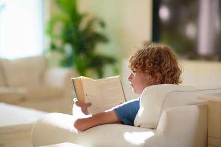 Child reading a book in sunny living room. Kid doing homework. Kids read books. Education and early development. School boy enjoying a story.の写真素材