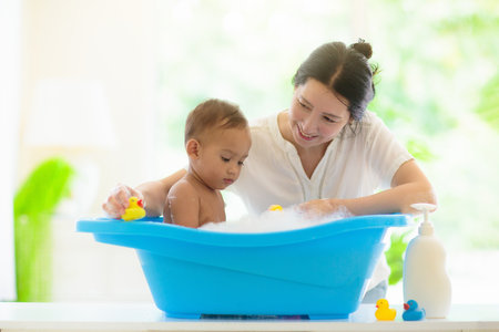 Baby boy in bath. Mother washing infant child. Cute little toddler playing with soap foam in white...
