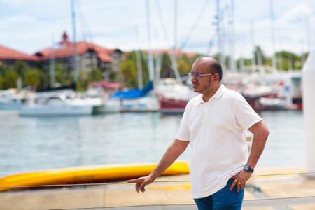 Young man walking in yacht club. Indian male tourist in tropical resort. Summer beach vacation on exotic island.の写真素材