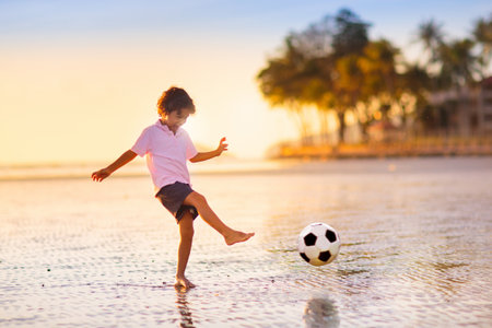 Kids play football on tropical beach at sunset. Cute little boy running with a ball. Travel with kids. Summer vacation on seashore. Family holidays with children. water sports fun.の写真素材