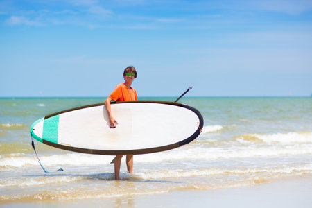 Young man standing up paddle board. Water fun and beach sport. Healthy outdoor sports for summer vacation on tropical island. holiday activity. Fit teenager boy training. Surfer exercising.の写真素材