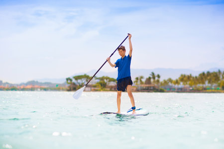 Child on stand up paddle board. Water fun and beach sport for kids. Little boy on surf board. Healthy outdoor sports for summer vacation on tropical island. holiday activity. Surfer exercising.の写真素材