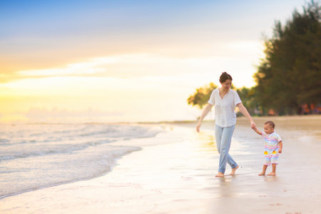 Mother and baby on tropical beach at sunset. Asian woman with infant boy walking and playing at sea. Young mom and little boy walk on ocean coast. Travel with kids. vacation with young child.の写真素材
