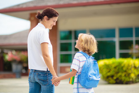mother bringing child to school. Parents pick up little boy after class. Young mom picking up kid after lessons in kindergarten or preschool. First day of school year. Kids happy to be back to school.の写真素材