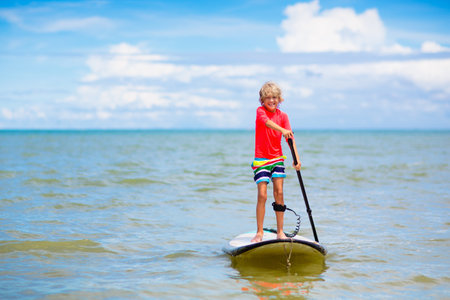 Child on stand up paddle board. Water fun and beach sport for kids. Little boy on surf board. Healthy outdoor sports for summer vacation on tropical island. holiday activity. Surfer exercising.の写真素材