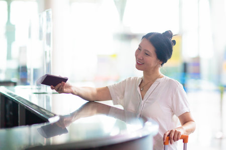 Young Asian woman in airport. Travel by air. Female walking inside airport terminal hall holding passport and boarding pass. vacation or business trip. girl with suitcase. Check in for holiday flight.の写真素材