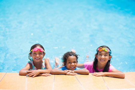 Kids play in swimming pool. Children learn to swim in outdoor pool of tropical resort during family summer vacation. Water and splash fun for young kid on holiday. Sun protection for child and baby.の写真素材