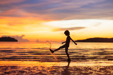Child playing on ocean beach. Kid jumping in the waves at sunset. Sea vacation for family. Little boy running on exotic island during summer holiday.の写真素材
