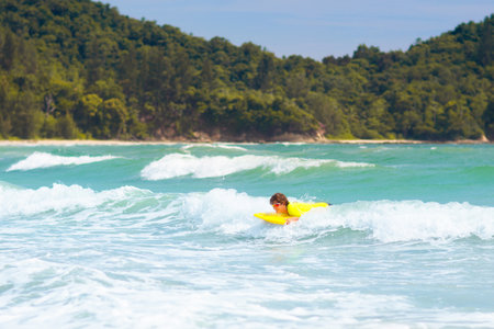 Teenage boy surfing on tropical beach. Family summer vacation in Asia. Kids swim in ocean water. Teenager on surf body board. Young adult swimming in exotic sea. Active water and beach sport.の写真素材