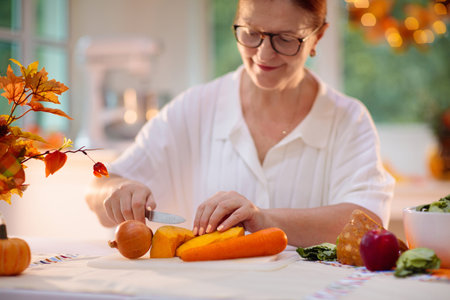 Thanksgiving dinner preparation. Woman cutting pumpkin, carrot and onion for autumn season pie. Decorated kitchen in Halloween season. Female cooking celebration feast. Seasonal vegetables.の写真素材