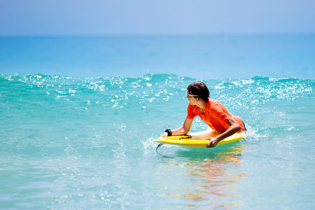 Teenager boy surfing on tropical beach in Asia. Child on surf board on ocean wave. Active water...