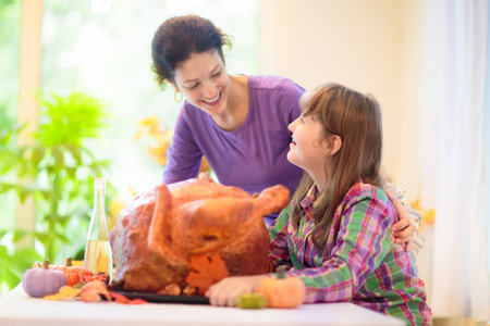 Turkey for Thanksgiving. Family cooking festive dinner. Girl roasting meat in decorated kitchen. Mother and kid cook in autumn. Fall season food.の写真素材