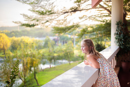 Child watching beautiful mountain and lake view from balcony or patio. Child on house deck. Garden backyard in summer.の写真素材