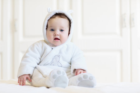 Adorable baby in white sunny bedroom. Newborn child relaxing in bed. Nursery for young children....