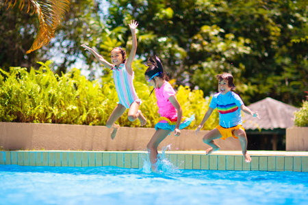Group of kids jump into swimming pool. Summer water fun. Children play in outdoor pool. Summer family vacation with young kid. Holiday in tropical resort. Travel with child.の写真素材