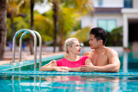 Pregnant woman in swimming pool on tropical beach holiday. Interracial couple expecting baby. Healthy and fit pregnancy. Active sport and fitness for expecting mom. Vacation before baby birth.の写真素材