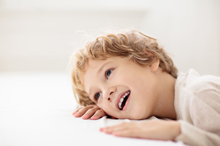 Child looking out of window and smiling. Little boy on white bed. Happy kid laughing and playing.の写真素材