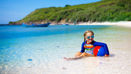 Kids playing on tropical beach. Children swim and play at sea on summer family vacation. Sand and water fun, sun protection for young child. Little girl running and jumping at ocean shore.の写真素材