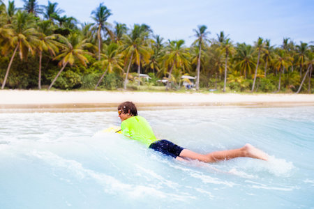 Teenage boy surfing on tropical beach. Family summer vacation in Asia. Kids swim in ocean water....