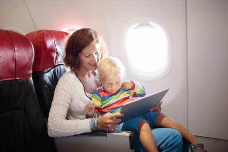 Child in airplane. Kid in air plane sitting in window seat. Flight entertainment for kids. Traveling with young children. Kids fly and travel. Family summer vacation. Little boy with toy in airplane.の写真素材