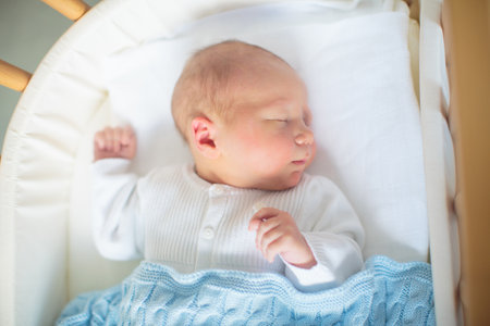 Newborn baby in hospital room. New born child in wooden co-sleeper crib. Infant sleeping in bedside bassinet. Safe co-sleeping in a bed side cot. Little boy taking a nap under knitted blanket.の写真素材