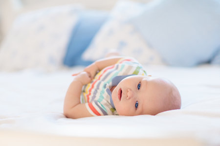 Adorable baby in white sunny bedroom. Newborn child relaxing in bed. Nursery for young children. Textile and bedding for kids. Family morning at home. New born kid during tummy time with toy bear.の写真素材