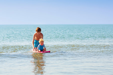 Kids playing on tropical beach. Water splash fun. Little boy splashing in sea waves. Children swim and play on summer family vacation. Sand and water toy, sun protection for young child.の写真素材