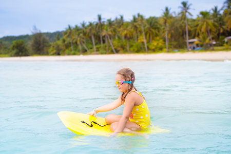 Child surfing on tropical beach. Family summer vacation in Asia. Kids swim in ocean water. Kid on surf body board. Little child swimming in exotic sea. Travel with children. Water and beach sport.の写真素材