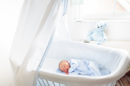 Baby playing in a white crib. Little child in bed. Bedding and furniture for kids nursery. Infant going to sleep. Nap for young kid. Sleepwear for children.の写真素材