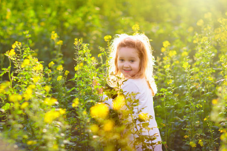 Cute little girl in white dress playing in blooming spring park with first white wild anemone flowers. Child on Easter egg hunt in blooming garden. Kids play outdoor picking flower bouquet.の写真素材