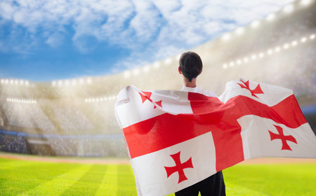 Georgia football supporter on stadium. Georgian fans on soccer pitch watching team play. Group of supporters with flag and national jersey cheering for Georgia. Championship game.の写真素材