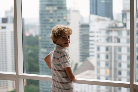 Child at a large window. Home safety. Safe lock on windows in high rise building apartment. Kids window protection. Beautiful view in city house.の写真素材