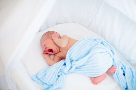 Adorable baby in white sunny bedroom. Newborn child relaxing in bed. Nursery for young children. Textile and bedding for kids. Family morning at home. New born kid during tummy time with toy bear.の写真素材